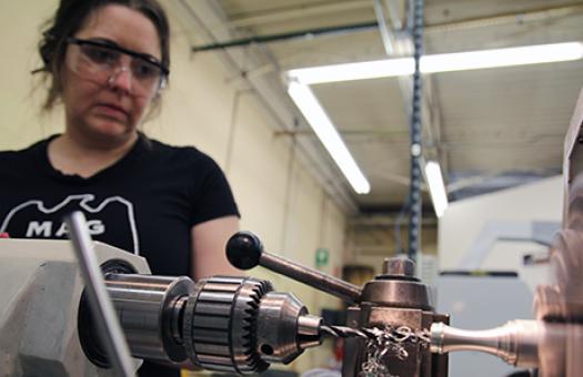 female student watches a grinder carve a metal piece