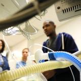 perspective from behind respiratory machine with plastic tubing and three out of focus students in background