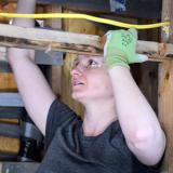 A female student in a construction trades course uses her left hand to steady herself as she looks upward into the rafters of a structure.