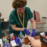 student wearing purple gloves and practicing putting needle in arm of mannequin