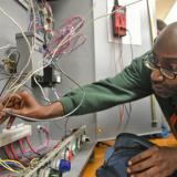 adult male student inserts wire into electrical board 