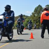 motorcyclists drive around orange cones while instructor supervises