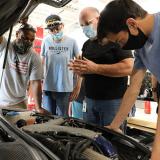 masked instructor and students look at auto engine in automotive lab