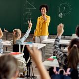 teacher standing in front of class calls on students with their hands raised