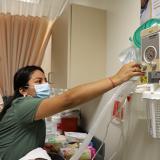 nursing student reaches above bed to adjust suction equipment